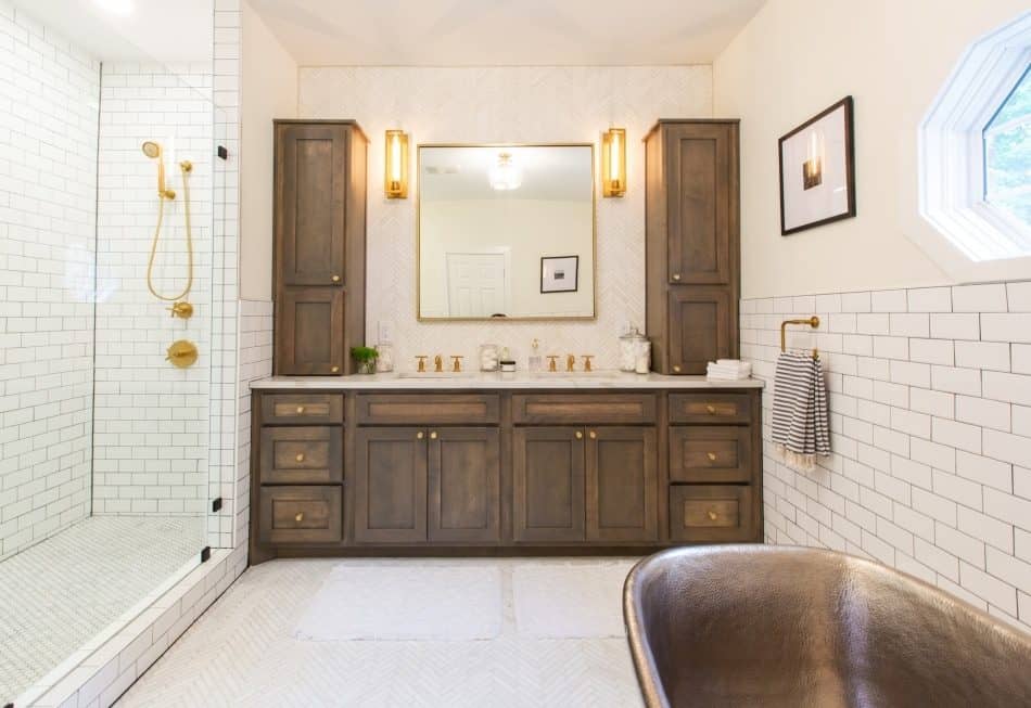 Bright bathroom with wooden vanity, gold fixtures, and a glass shower
