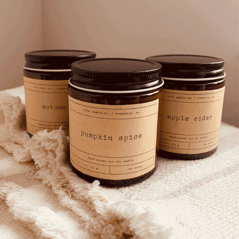 Amber jar candles labeled pumpkin spice, apple cider, and autumn on cozy fabric