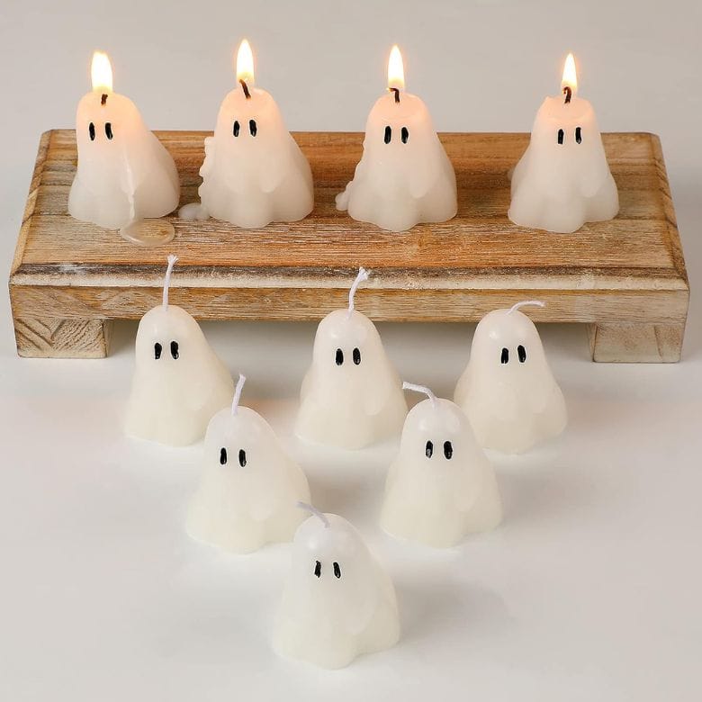 Ghost-shaped candles, some lit, displayed on a wooden stand and table