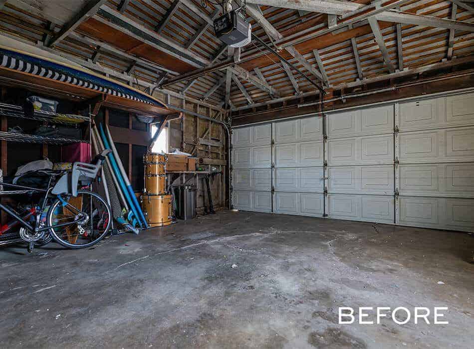 A before image of a cluttered garage with a concrete floor, exposed rafters, and a white garage door