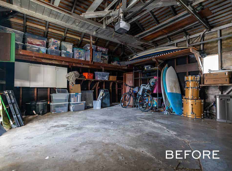 Cluttered garage with shelves of storage bins, surfboards, bicycles, drums, and miscellaneous items