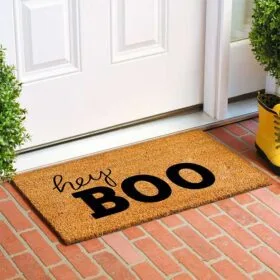 Doormat with "hey BOO" text at brick porch entry with yellow boots