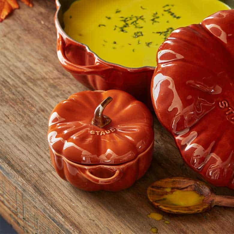 Pumpkin-shaped ceramic cocottes filled with soup on a rustic wooden table