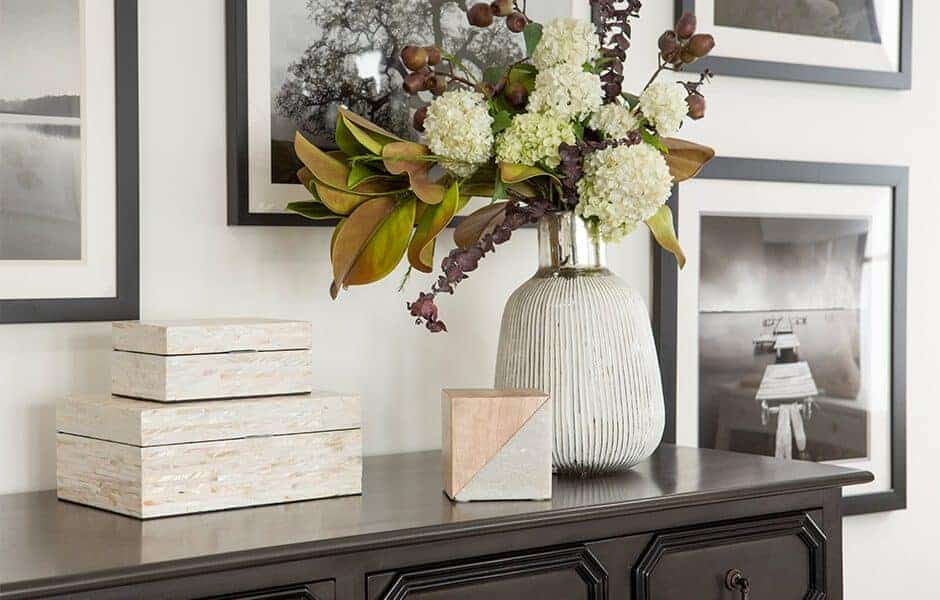 Elegant console table with decorative boxes, a ceramic vase of white flowers, and black-and-white framed wall art.
