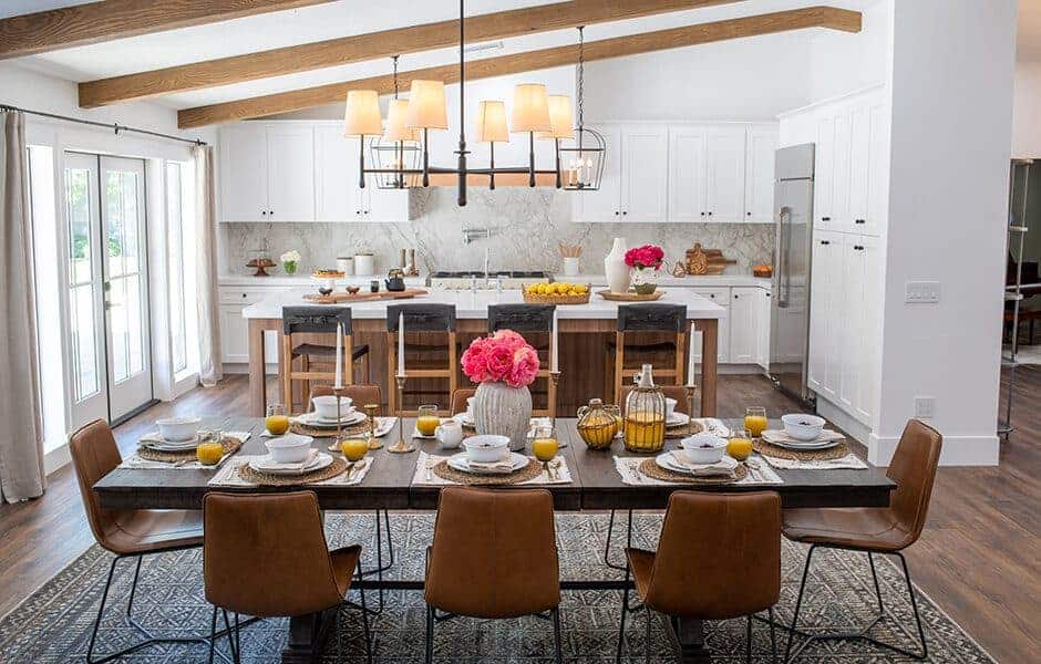 Dining area with a rustic table, leather chairs, and a bright kitchen with white cabinets and wood beams