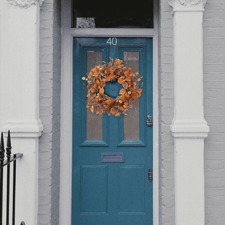 A teal door with a white frame and a white wreath hanging on it