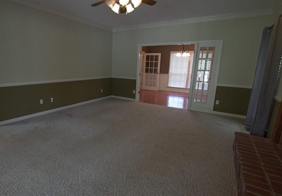 Spacious and empty living room with carpeted floors and a fireplace featuring french doors that lead to a dining room