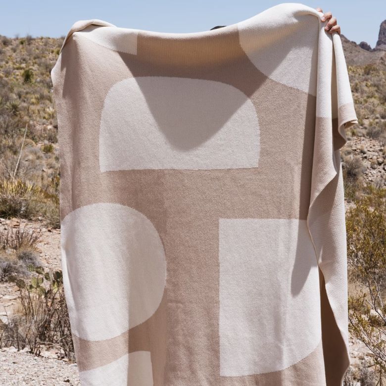 Beige and cream blanket with abstract geometric shapes held outdoors in a desert landscape