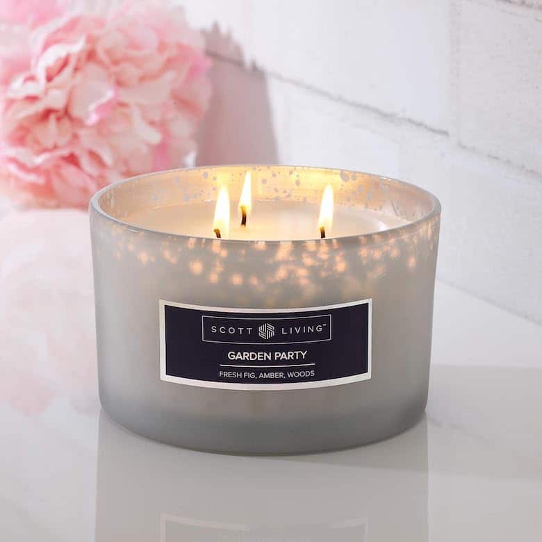 Lit three-wick candle in frosted glass container with floral background