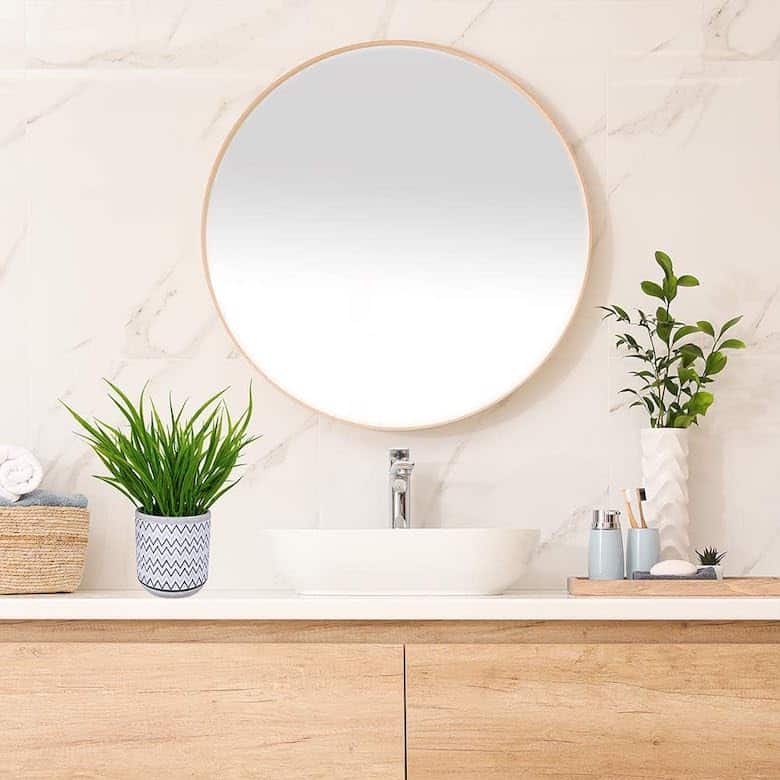 Bright bathroom vanity with round mirror, wood cabinets, and potted plants on a white countertop