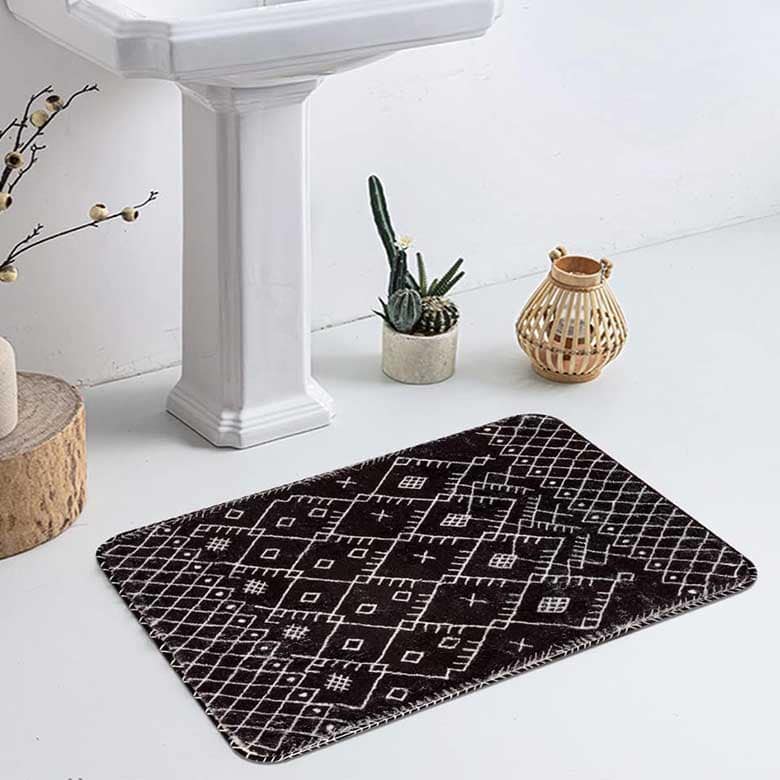 Black and white geometric bath mat beside pedestal sink with decorative accents