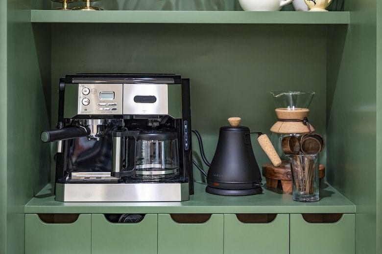 Coffee station with espresso maker, gooseneck kettle, Chemex, and coffee accessories on green shelf