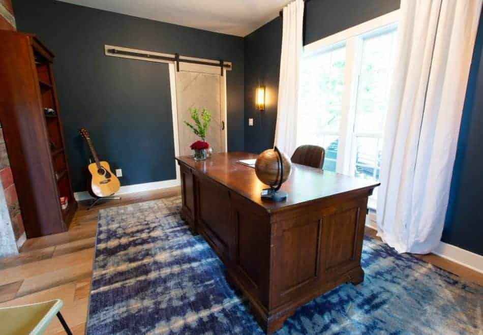 Home office with a dark blue wall, a sliding barn door, and a large wooden desk
