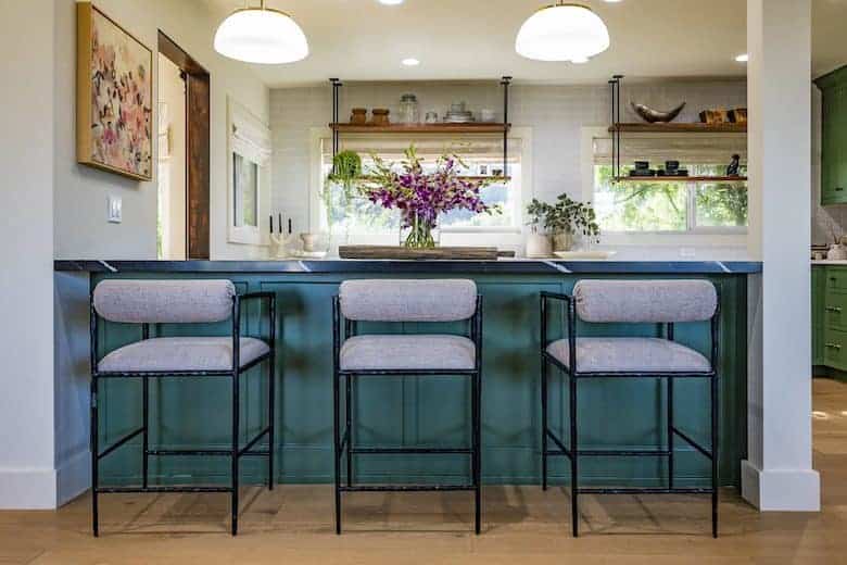 Kitchen with a green island, upholstered barstools, and open shelving