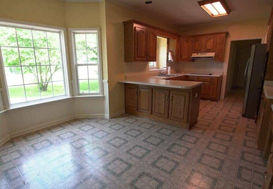 Kitchen with wood cabinets, patterned linoleum flooring, and a large bay window letting in natural light