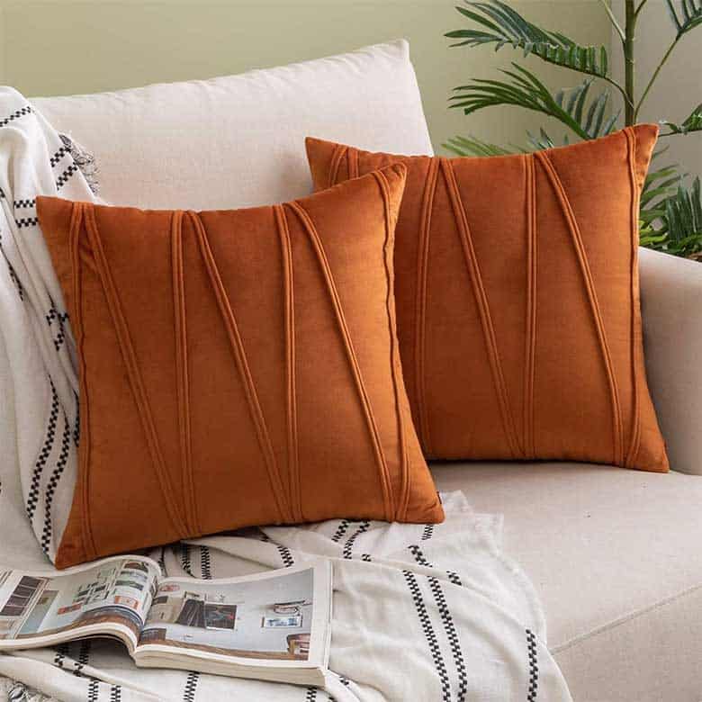 Two orange decorative pillows on a cream sofa with a striped throw and open magazine