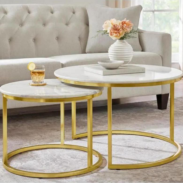 Nested round coffee tables with white marble tops and gold metal frames in front of a tufted sofa