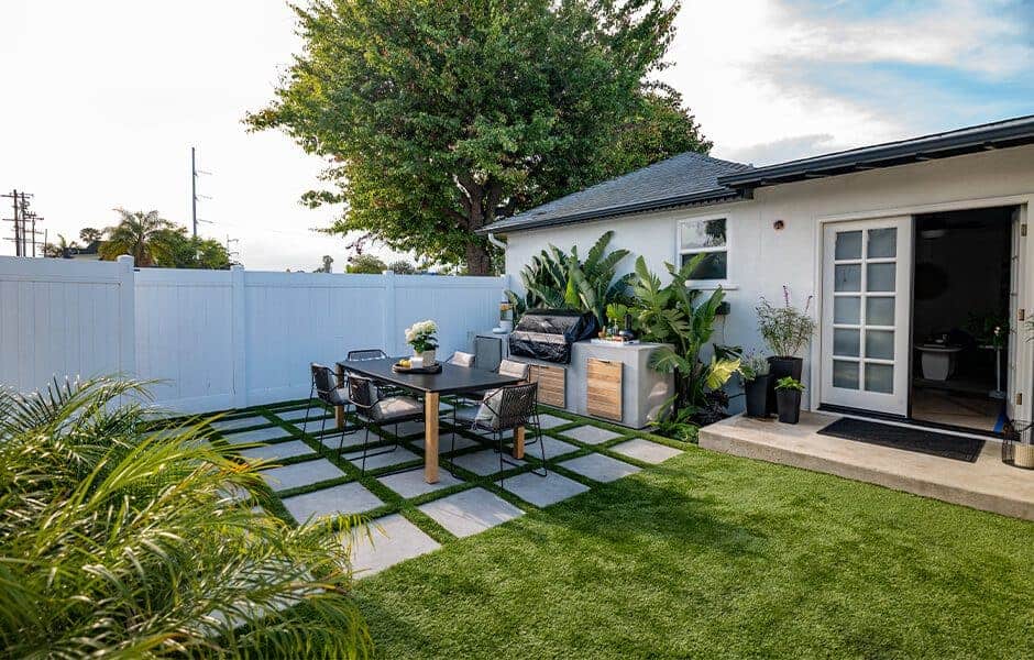 Backyard patio with a dining table, barbecue area, and lush greenery on grass