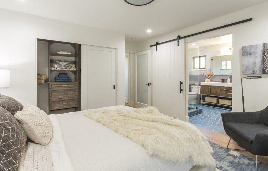 Modern bedroom with white bed, sliding barn door to bathroom, closet, and armchair