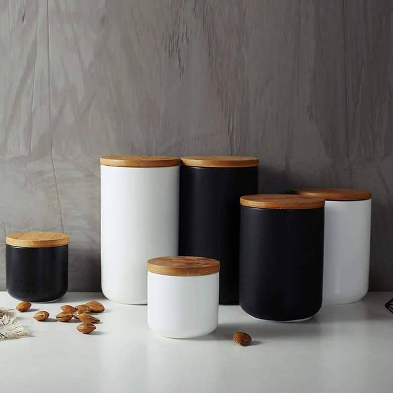 Black and white storage canisters with wooden lids on a countertop