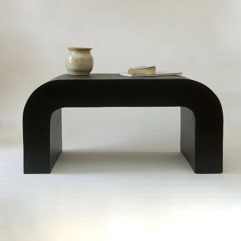 Black arched coffee table with a ceramic vase and books on top against a neutral background