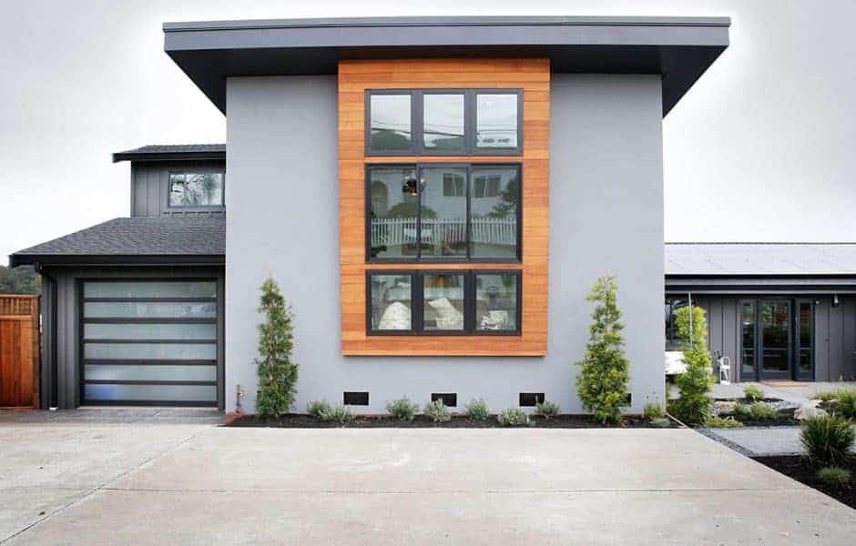 Two-story house with a gray stucco exterior and a wood-paneled accent wall featuring large windows