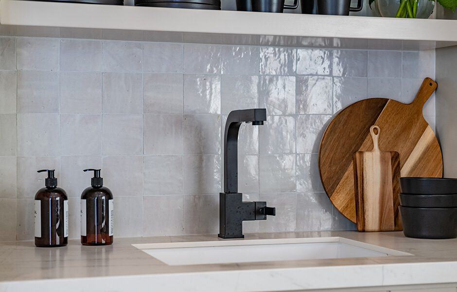 Modern kitchen sink area with a black faucet, wooden cutting boards, and tile backsplash