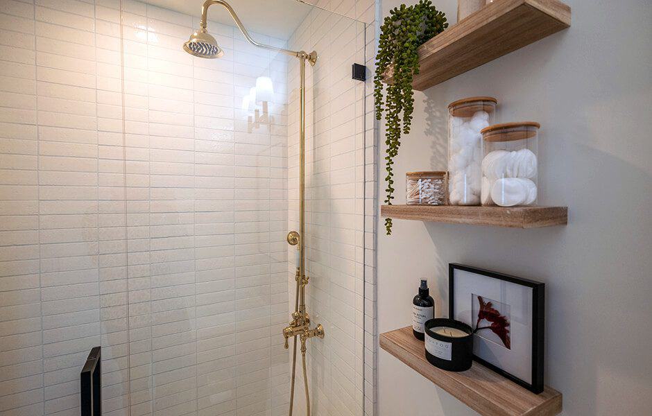 Minimalistic bathroom with white subway tiles, a gold-toned shower fixture, and wooden shelves