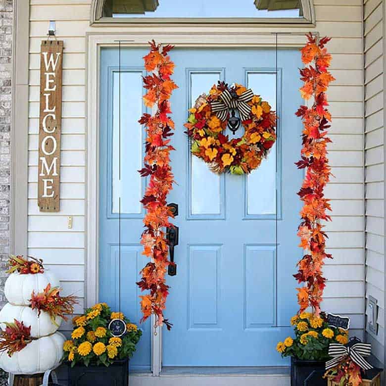 Fall front door decor with a blue door, autumn leaf garlands, and a wreath