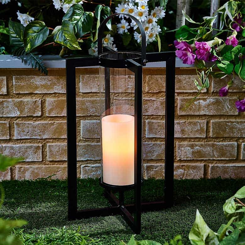Black outdoor lantern with cylindrical candle on artificial grass