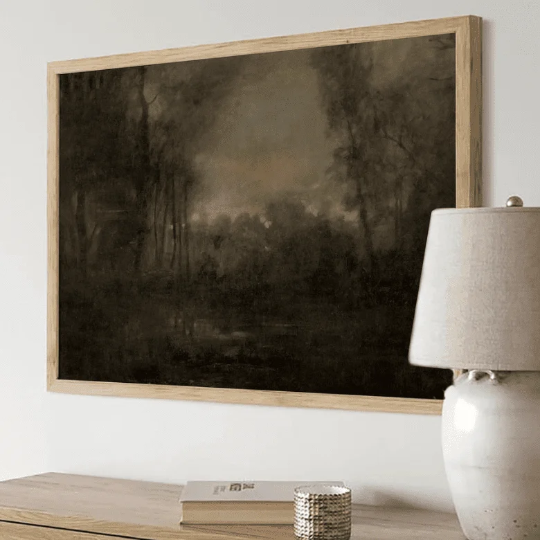 Framed dark landscape painting above a console with a lamp and decor items.