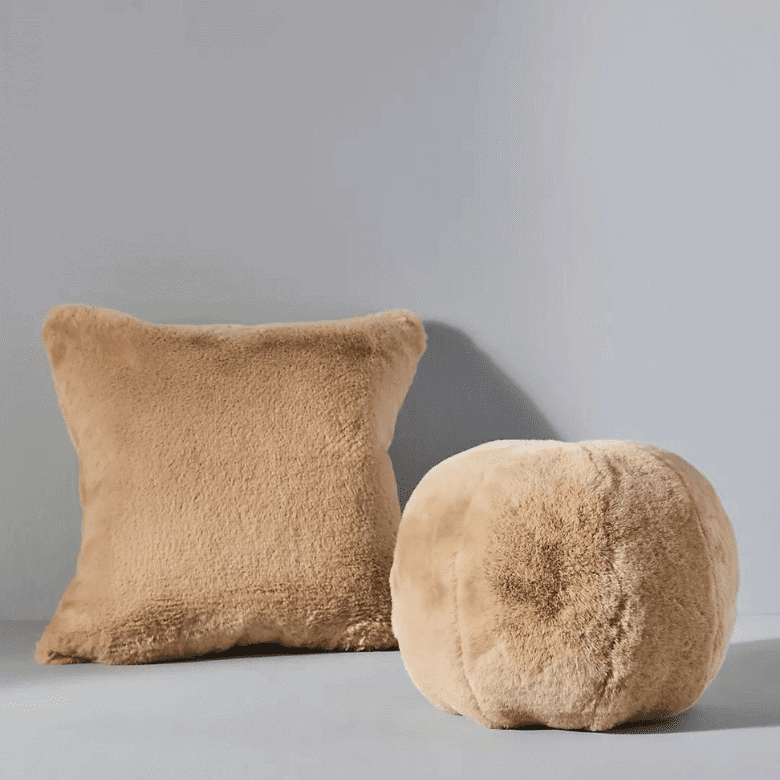 Tan faux fur pillow and matching round cushion on a neutral background