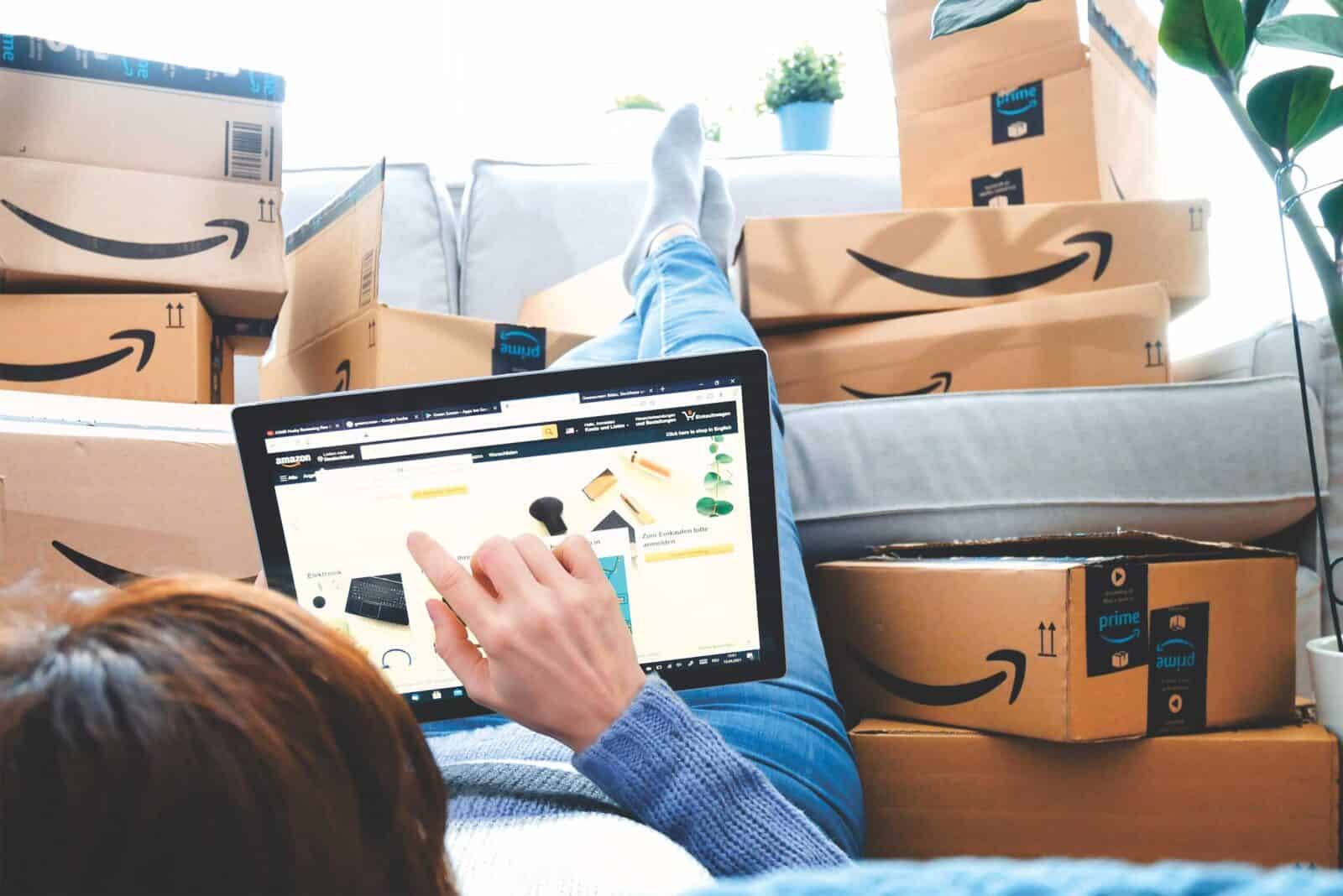 Person shopping on Amazon with a tablet while surrounded by stacked Prime delivery boxes