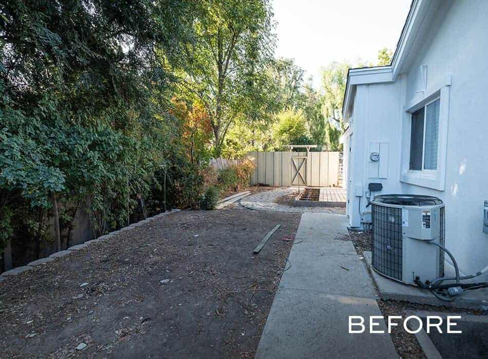 Backyard space with untended dirt, bordered by trees and a side view of a house