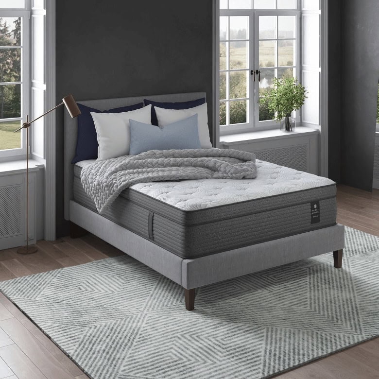 A bedroom with a gray upholstered bed, neatly made with pillows, a textured blanket, and a large window in the background