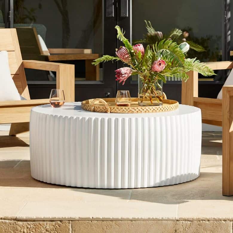 Outdoor setting with a round white coffee table, wooden chairs, and a floral arrangement with drinks