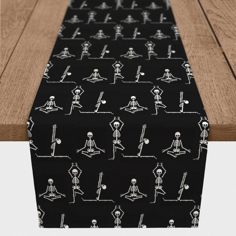 Black table runner with playful skeleton yoga pattern on a wooden table