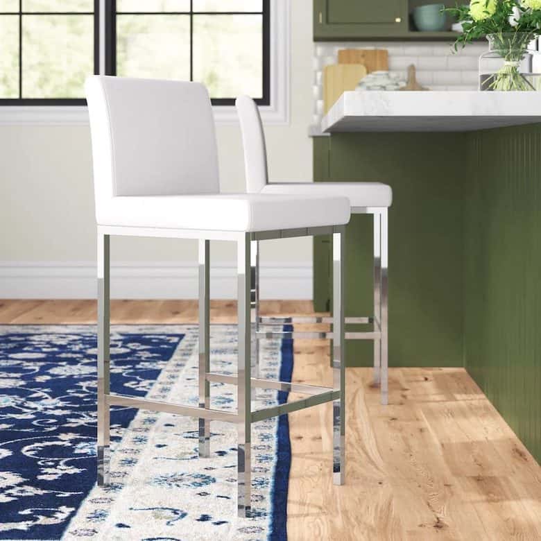 White upholstered bar stools with chrome legs at a green kitchen island on a blue patterned rug