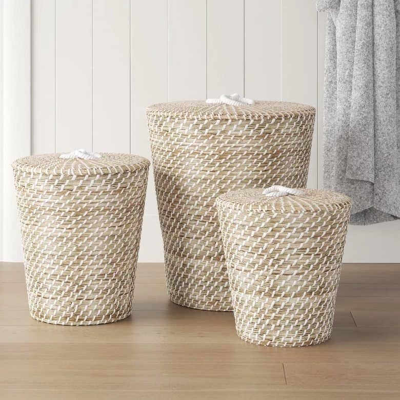 Set of three woven storage baskets with lids displayed on a wooden floor against a white paneled wall