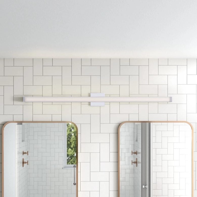 Modern bathroom with long LED vanity light, two arched mirrors, and white geometric tile wall
