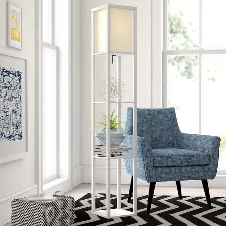 Modern reading nook with a blue accent chair, tall white shelf floor lamp, and geometric rug