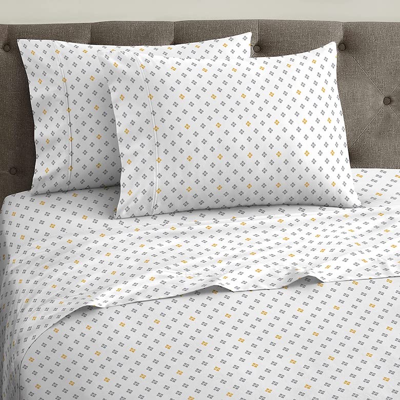 White bed sheet set with a small geometric pattern in gray and yellow on a tufted headboard bed