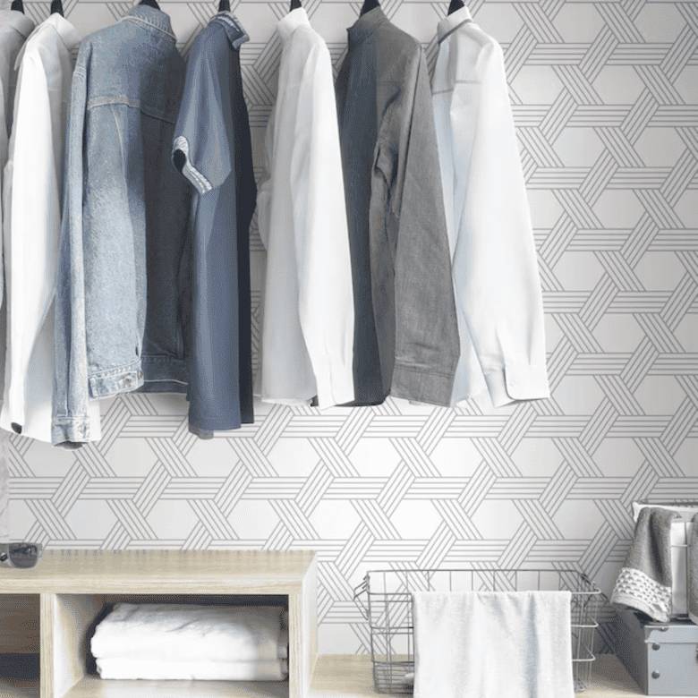 Minimalist closet with hanging shirts, geometric wallpaper, and wire laundry basket.