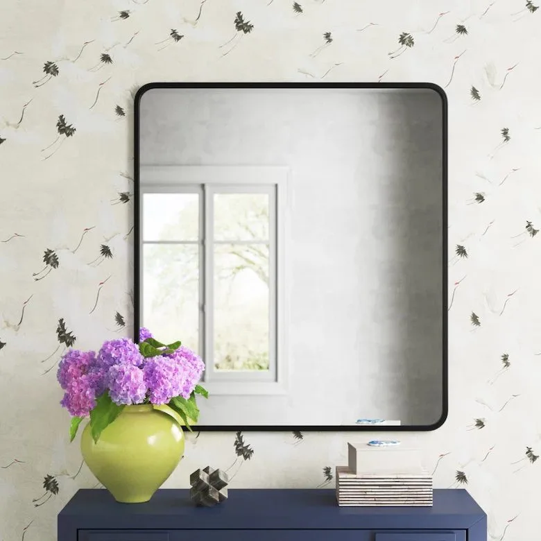 Mirror with black frame, purple flowers in a green vase, books, and a geometric object on a blue dresser