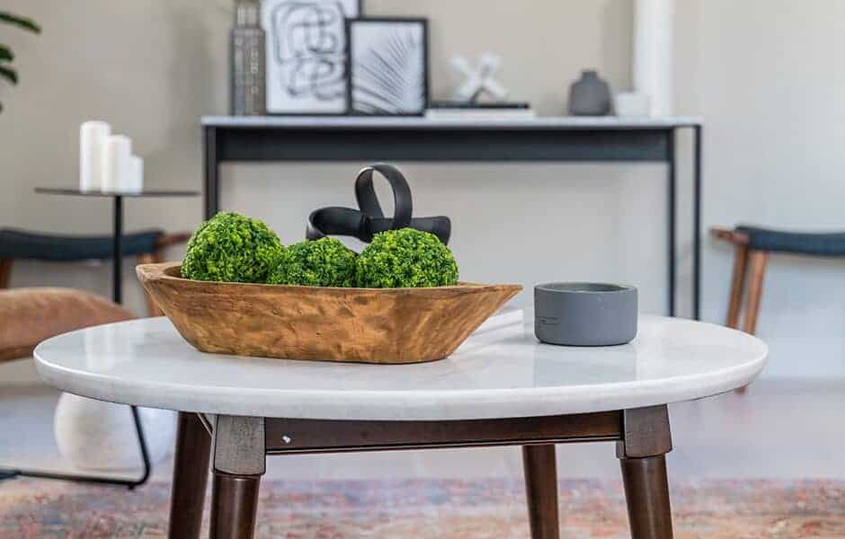 White marble coffee table with a wooden bowl holding green moss balls in a modern living room