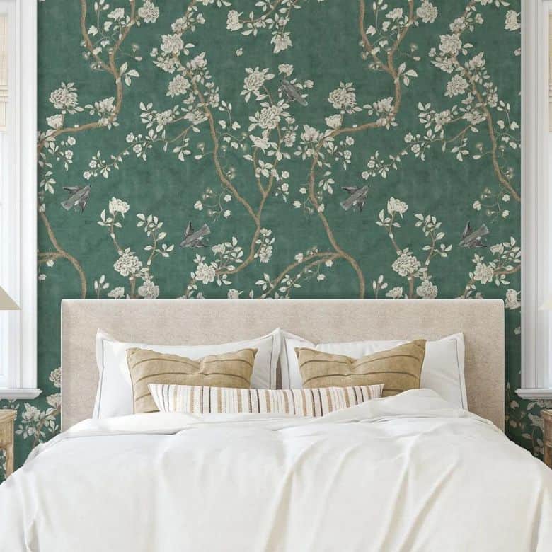 Bedroom with a light beige bed, adorned with pillows, against a floral green wallpaper featuring birds perched on branches