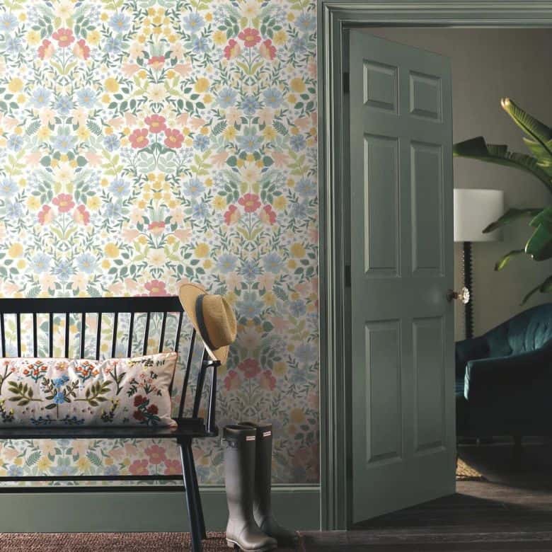 Vibrant floral wallpapered entryway with a black bench, embroidered pillow, and green door