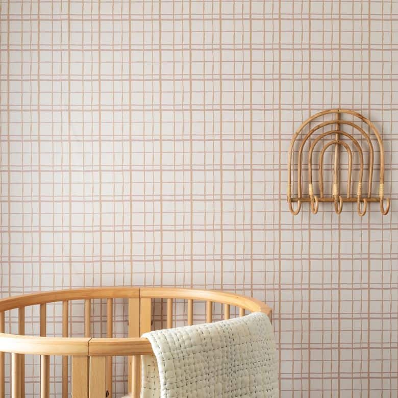 Nursery corner with round crib, grid wallpaper, and rattan hooks
