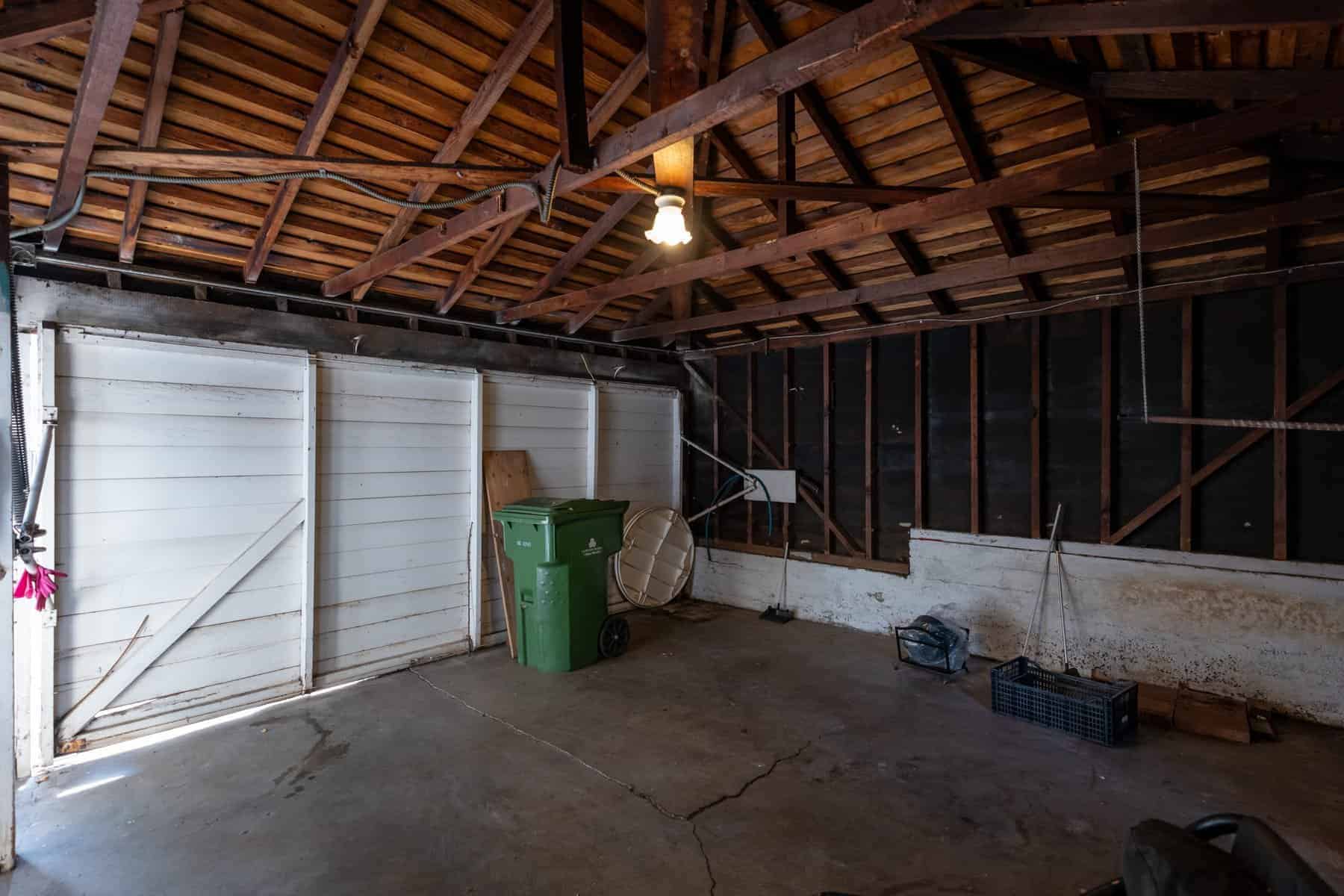 Old garage interior with exposed beams, concrete floor, and minimal storage items