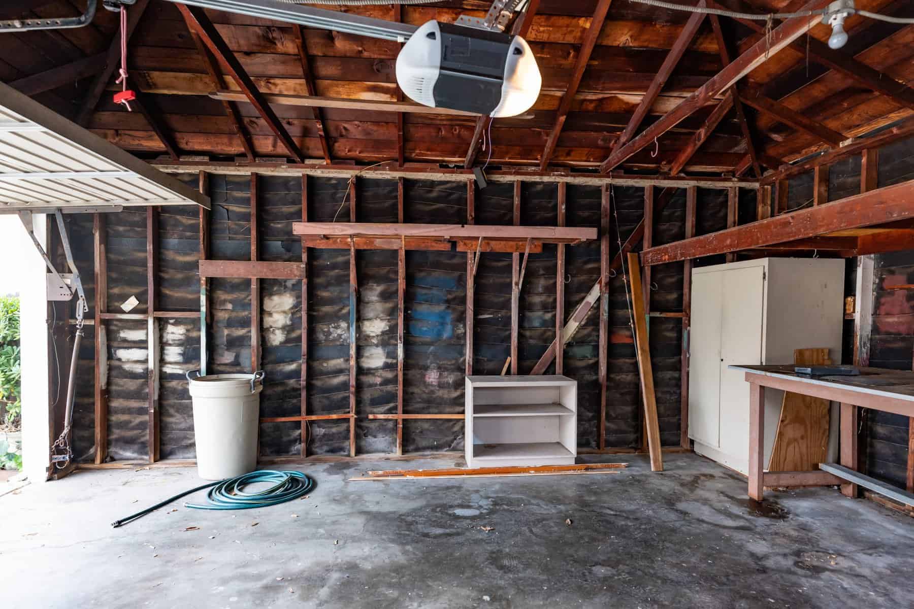 Empty garage with exposed wooden beams, a shelf, a bucket, a garden hose, and a workbench